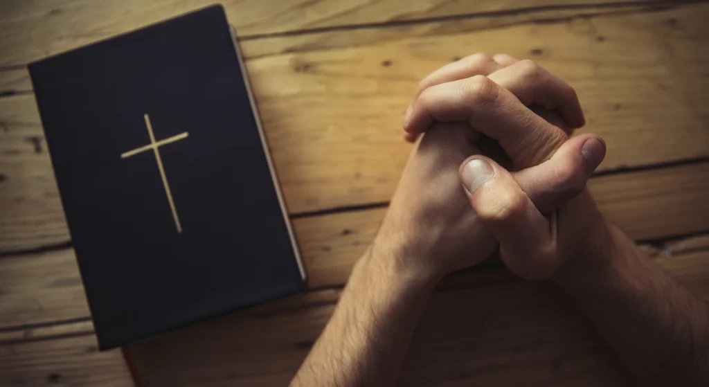 hands folded praying next to a Bible
